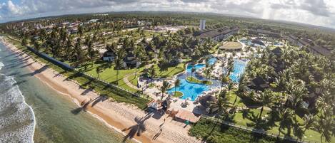 An aerial view of a resort with a large swimming pool, beachfront, and lush greenery.