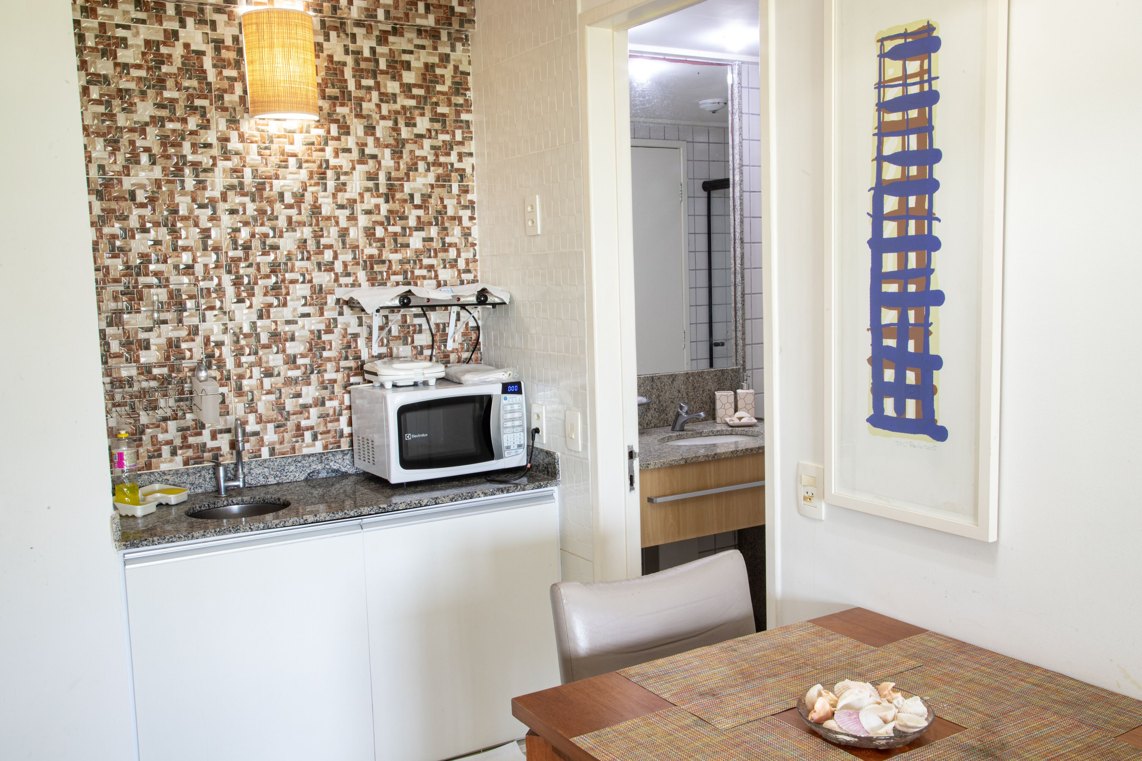 Una cocina compacta con microondas, pileta y un pequeño comedor con mesa y sillas.