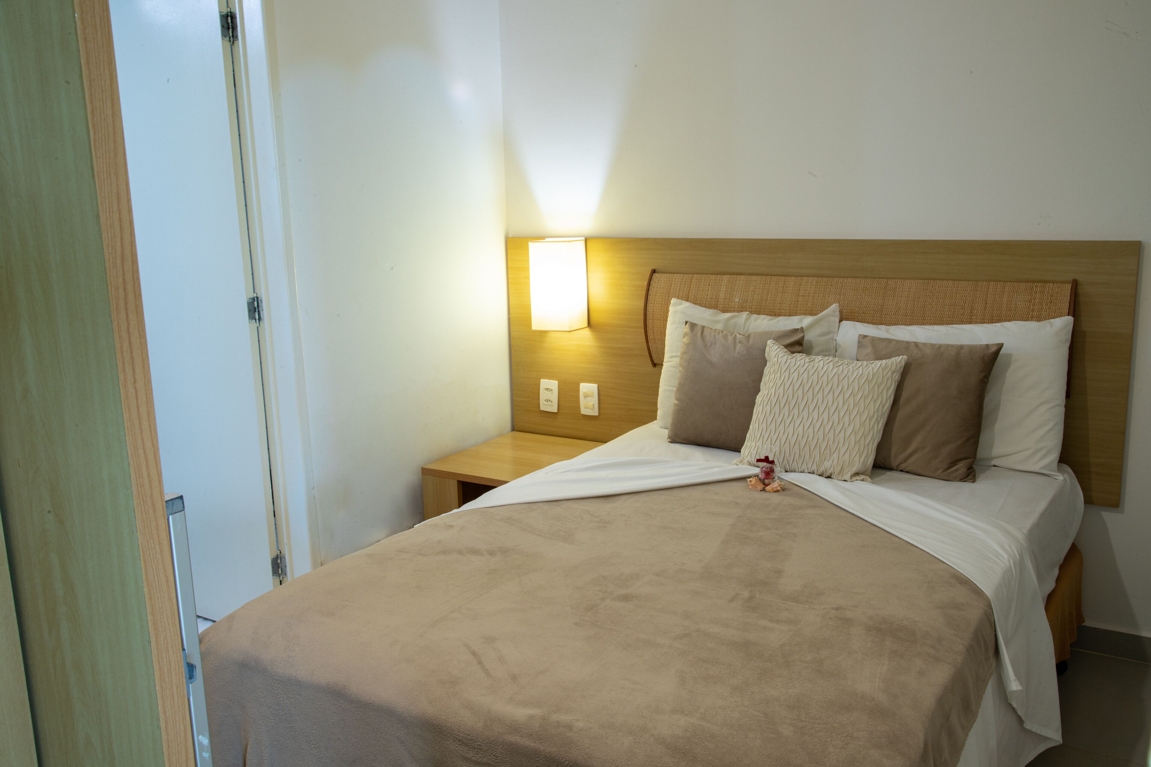 Une chambre d’hôtel avec un lit, une table de chevet, une lampe fixée au mur et une porte.