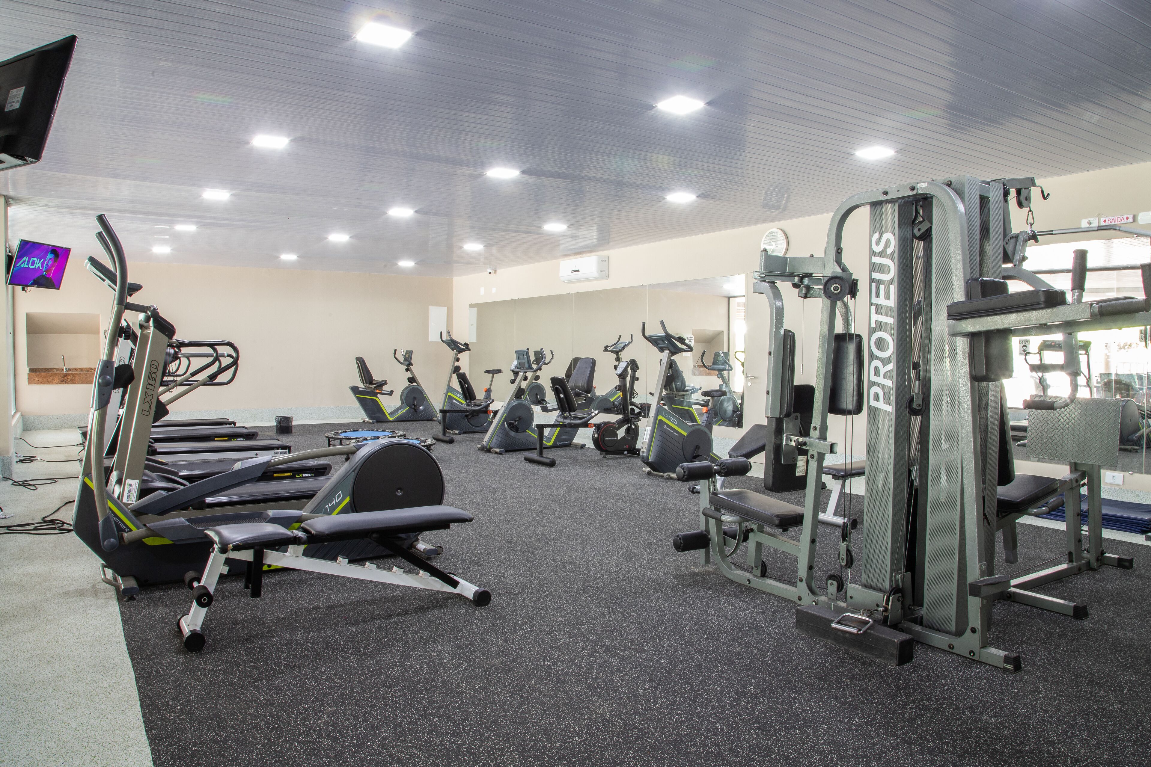 A gym with various exercise machines, including treadmills and weight stations, arranged in rows.