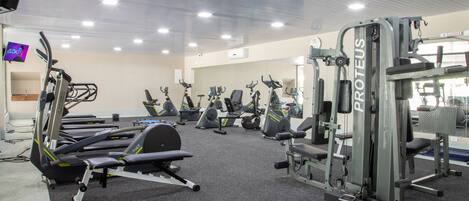 Un gimnasio con diferentes máquinas de ejercicio, incluyendo cintas de correr y pesas, dispuestas en filas.
