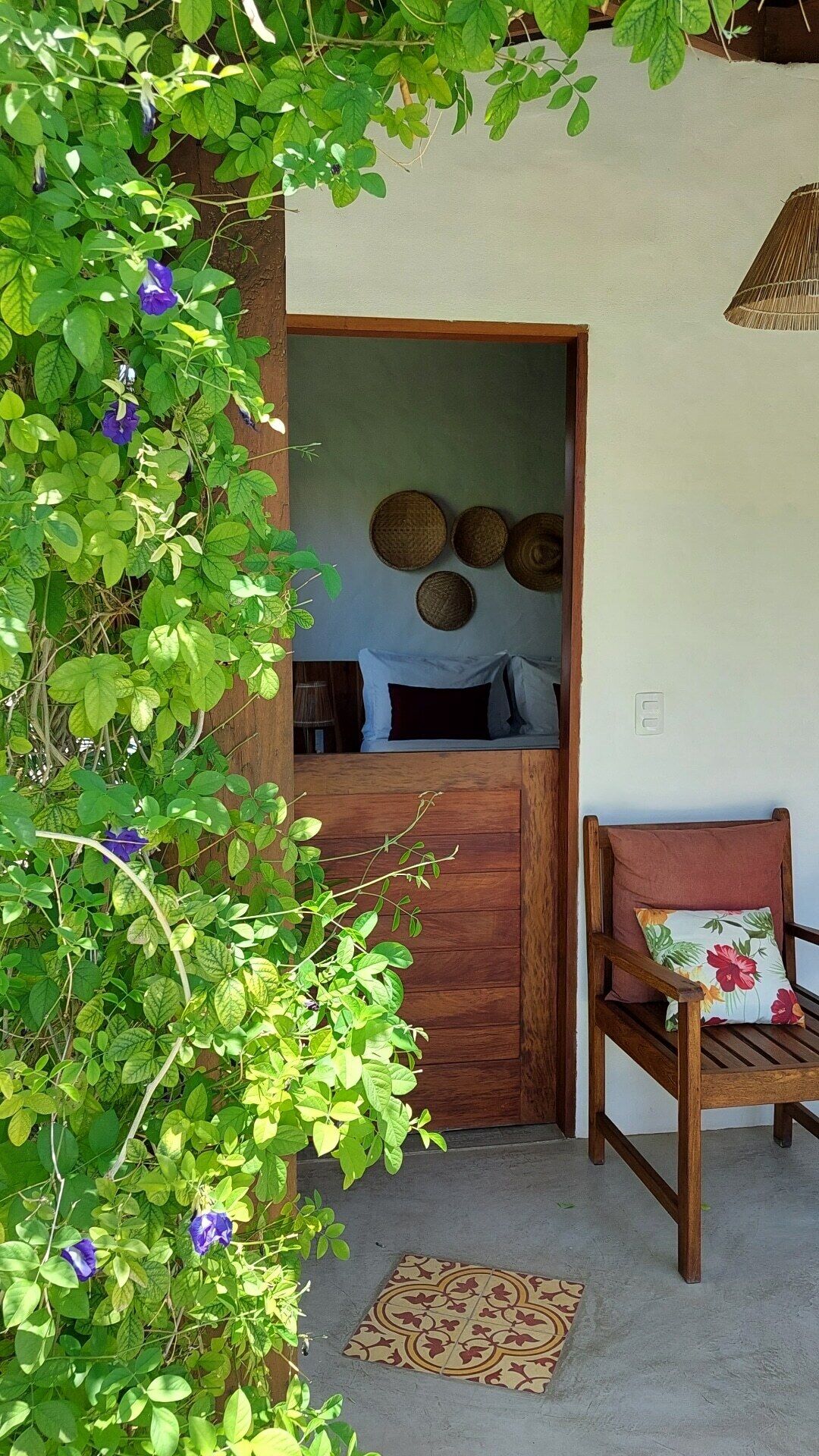 Una habitación con puerta de madera, una cama con ropa de cama blanca y negra, un tapiz de pared tejido y una silla con cojín floral.