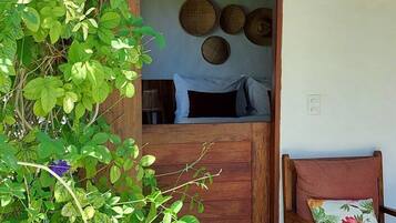 Una habitación con puerta de madera, una cama con ropa de cama blanca y negra, un tapiz de pared tejido y una silla con cojín floral.