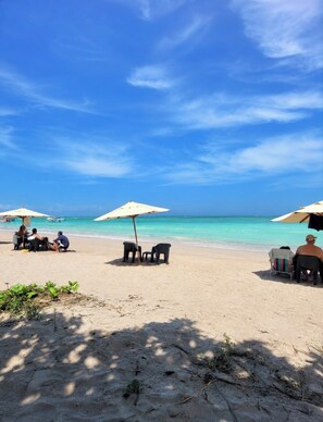 Una playa con cielos despejados, sombrillas y gente relajándose.