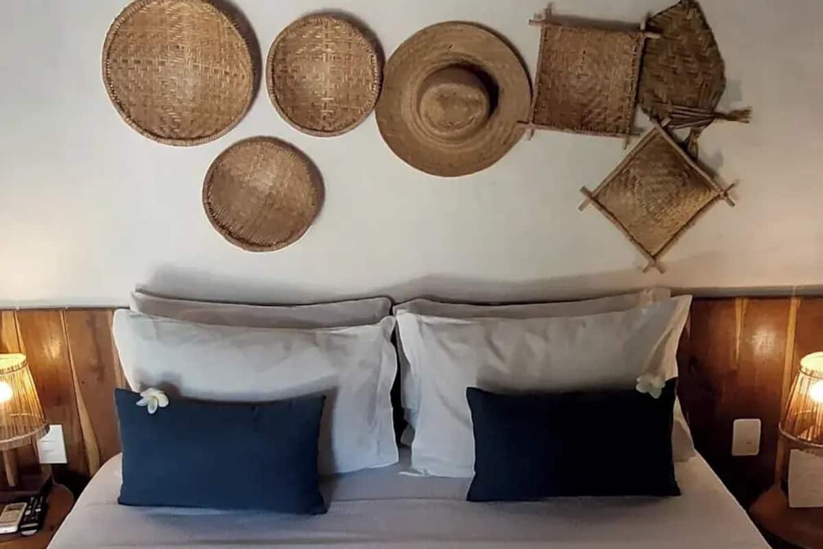 A bed with white and dark blue pillows, a white duvet, and a wall with woven baskets.