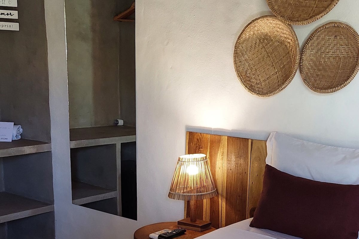 A hotel room with a bed, a nightstand with a lamp, a wardrobe, and three woven wall decorations.