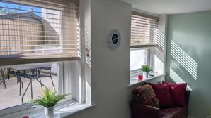 Une pièce avec une fenêtre, une horloge, une plante et un canapé rouge.