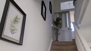 Un escalier recouvert d’une moquette beige et doté de rampes blanches, menant à une pièce avec une porte et une plante.