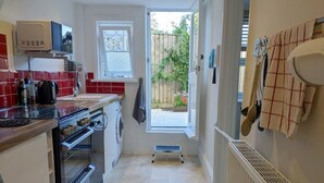 Une cuisine compacte équipée d’un four à micro-ondes, d’un four et d’un lave-linge. Un petit marchepied est placé près de la porte.