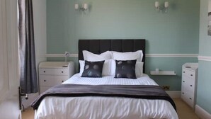 Une chambre à coucher comprenant un lit, deux tables de chevet, une commode et une lampe fixée au mur.