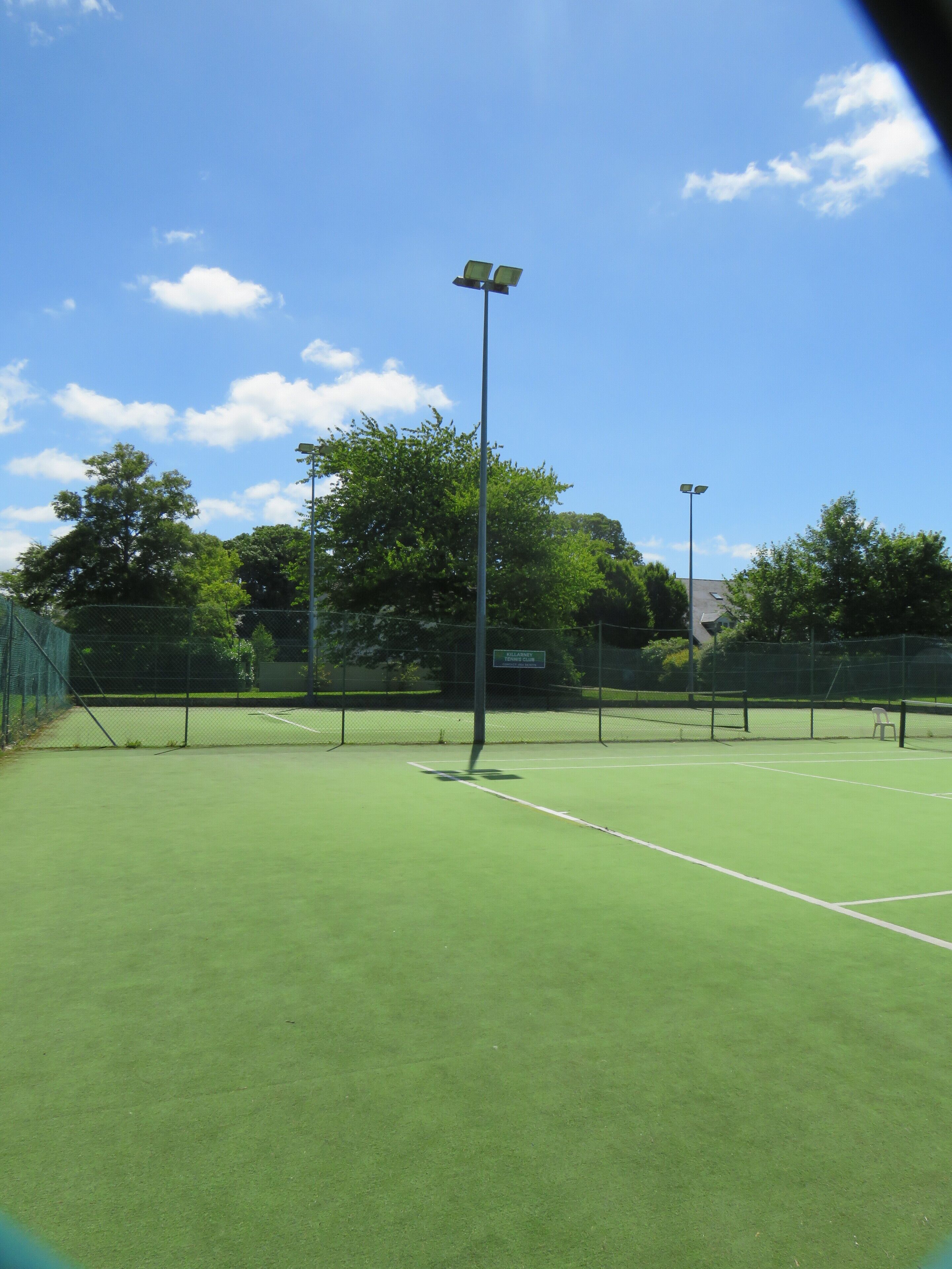 A tennis court with a net, surrounded by a fence, and a sign indicating it is part of a tennis club.