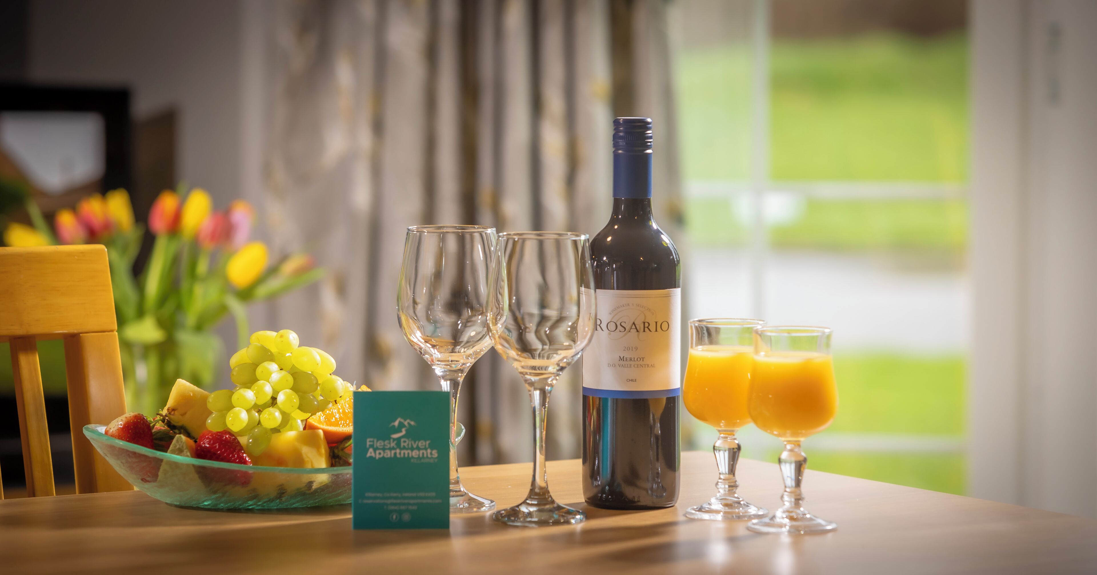 A table with a bottle of rosé wine, two glasses, a bowl of fruit, and a room service card.