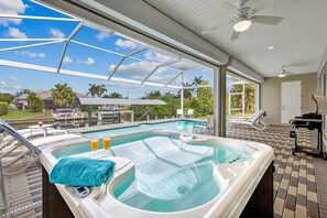 A hot tub with a towel and two glasses of orange juice, a pool, and a covered patio area with chairs and a table. - Modern, child-friendly villa with heated pool, right on the water with boat lift (Cape Coral)