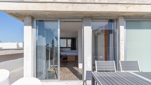 A balcony with a table and chairs, a sliding glass door leading to a bedroom with a bed and a chair, and a view of the sky. - Secret Garden by TLV2RENT (Tel Aviv)