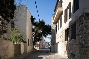 A narrow street lined with buildings, some with balconies and shutters, under a clear sky.
