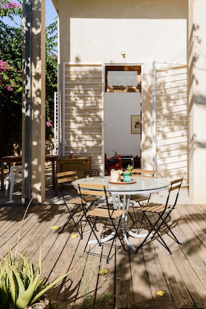 An outdoor patio with a round table and chairs, surrounded by wooden deck flooring and potted plants.