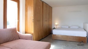 A bedroom with a bed, wooden wardrobe, and a pink sofa. - Secret Garden by TLV2RENT (Tel Aviv)