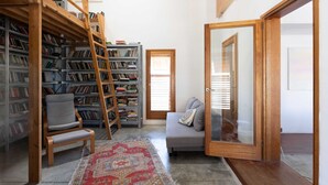 A library with bookshelves, a ladder, a chair, a sofa, and a patterned rug. - Secret Garden by TLV2RENT (Tel Aviv)