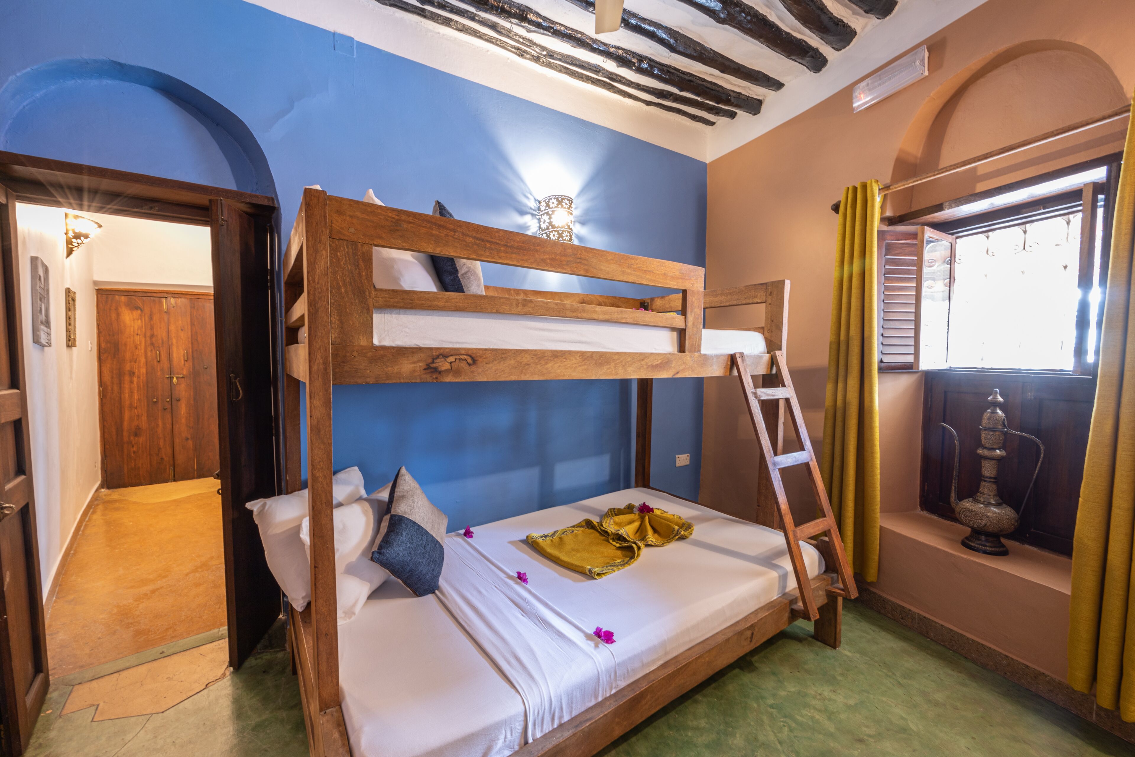 A bunk bed with a ladder, a window with curtains, and a decorative item on the windowsill.