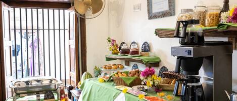 A breakfast buffet with various food items, a coffee machine, and a fan.