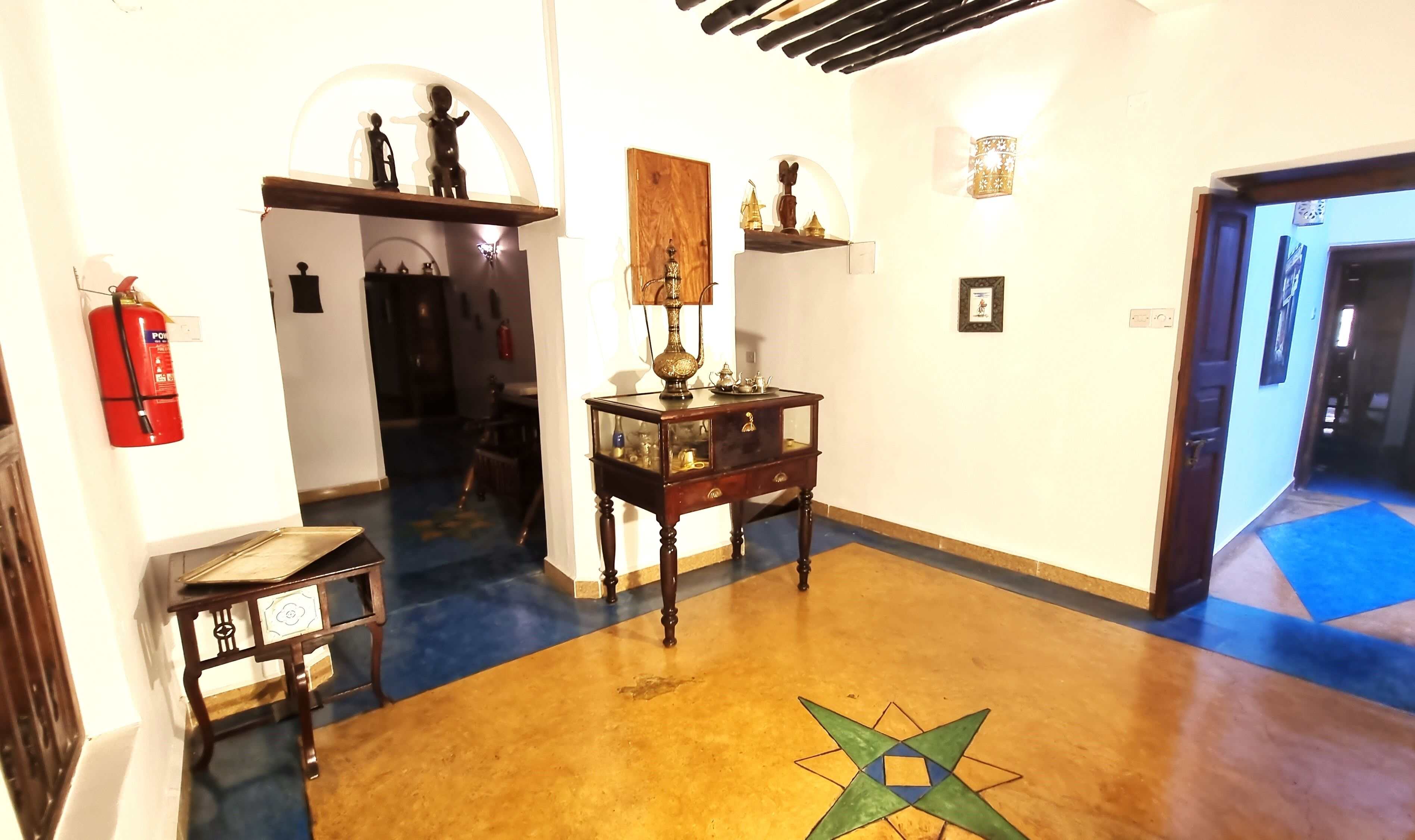 A hallway with a wooden floor, a glass display cabinet, a red fire extinguisher, and a door leading to another room.