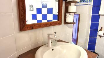 Un baño con lavamanos blanco, tocador de madera, espejo con marco decorativo y paredes con azulejos azules y blancos.