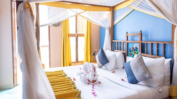 Una cama con sábanas blancas, cabecera de madera y pared azul.