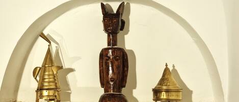 A shelf with three objects: a brass lamp, a wooden sculpture, and a golden urn.