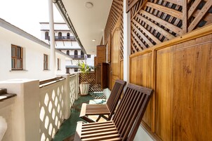 Un pasillo estrecho con bancos de madera y una cerca de celosía, que conduce a un edificio con balcones.