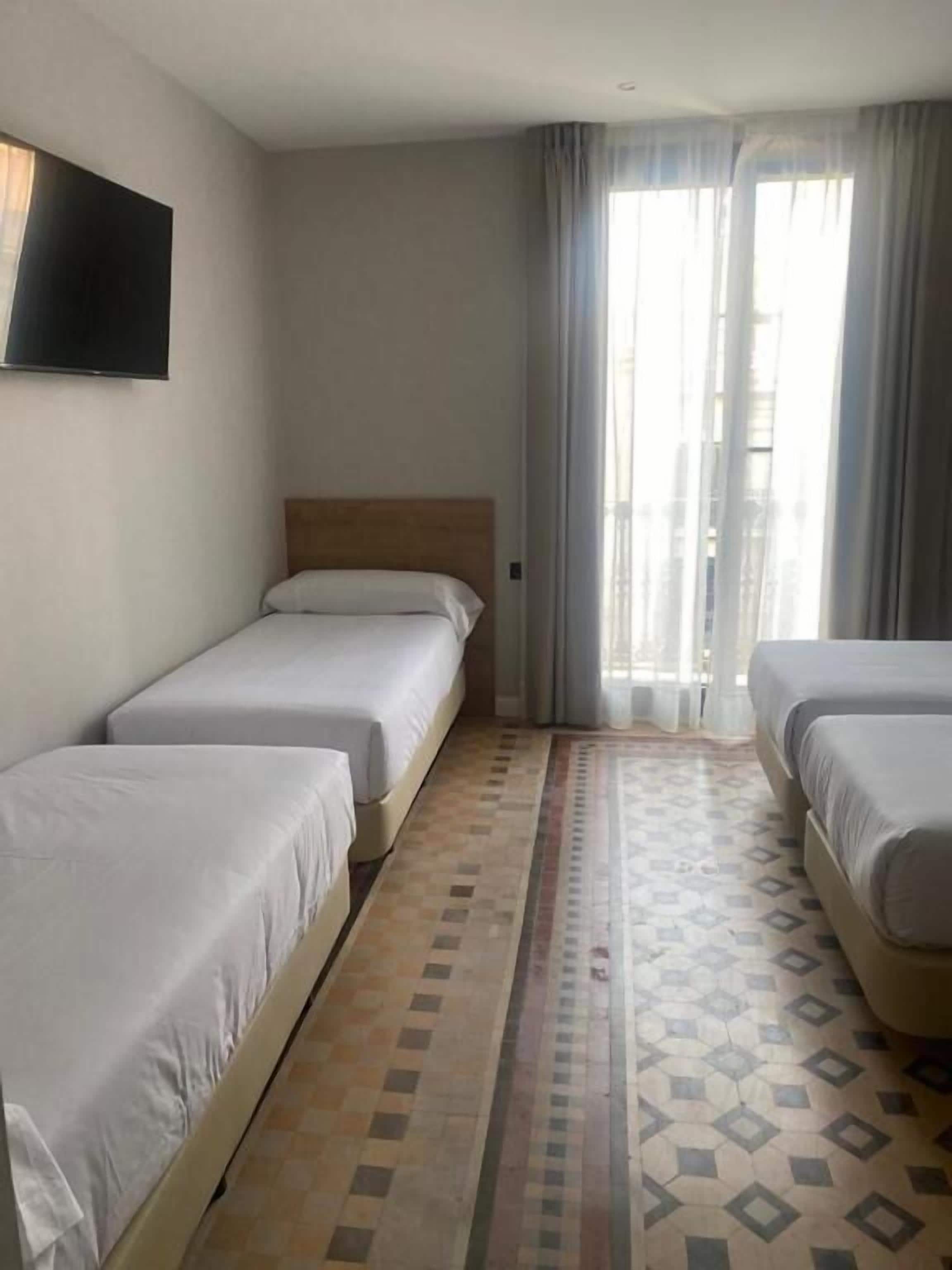 Una habitación de hotel con dos camas individuales, un televisor en la pared y un gran ventanal con cortinas.