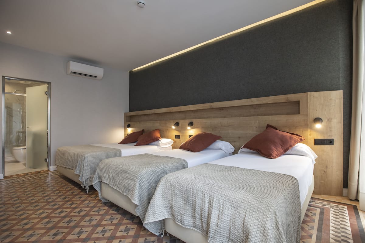 Habitación de hotel con tres camas, ducha y piso estampado.