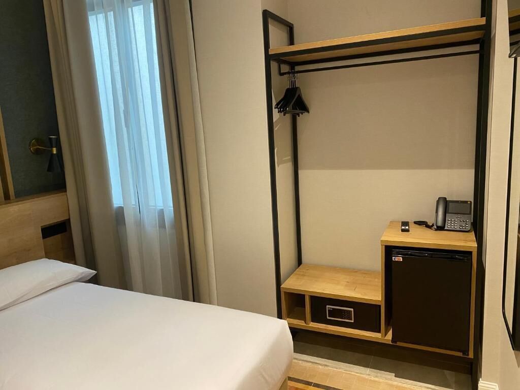 Habitación de hotel compacta con literas, un escritorio pequeño con teléfono y un refrigerador compacto.
