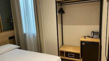 Habitación de hotel compacta con literas, un escritorio pequeño con teléfono y un refrigerador compacto.