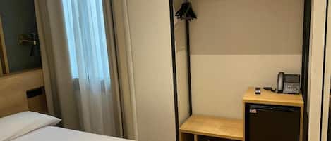 A compact hotel room with a bunk bed, a small desk with a telephone, and a compact refrigerator.