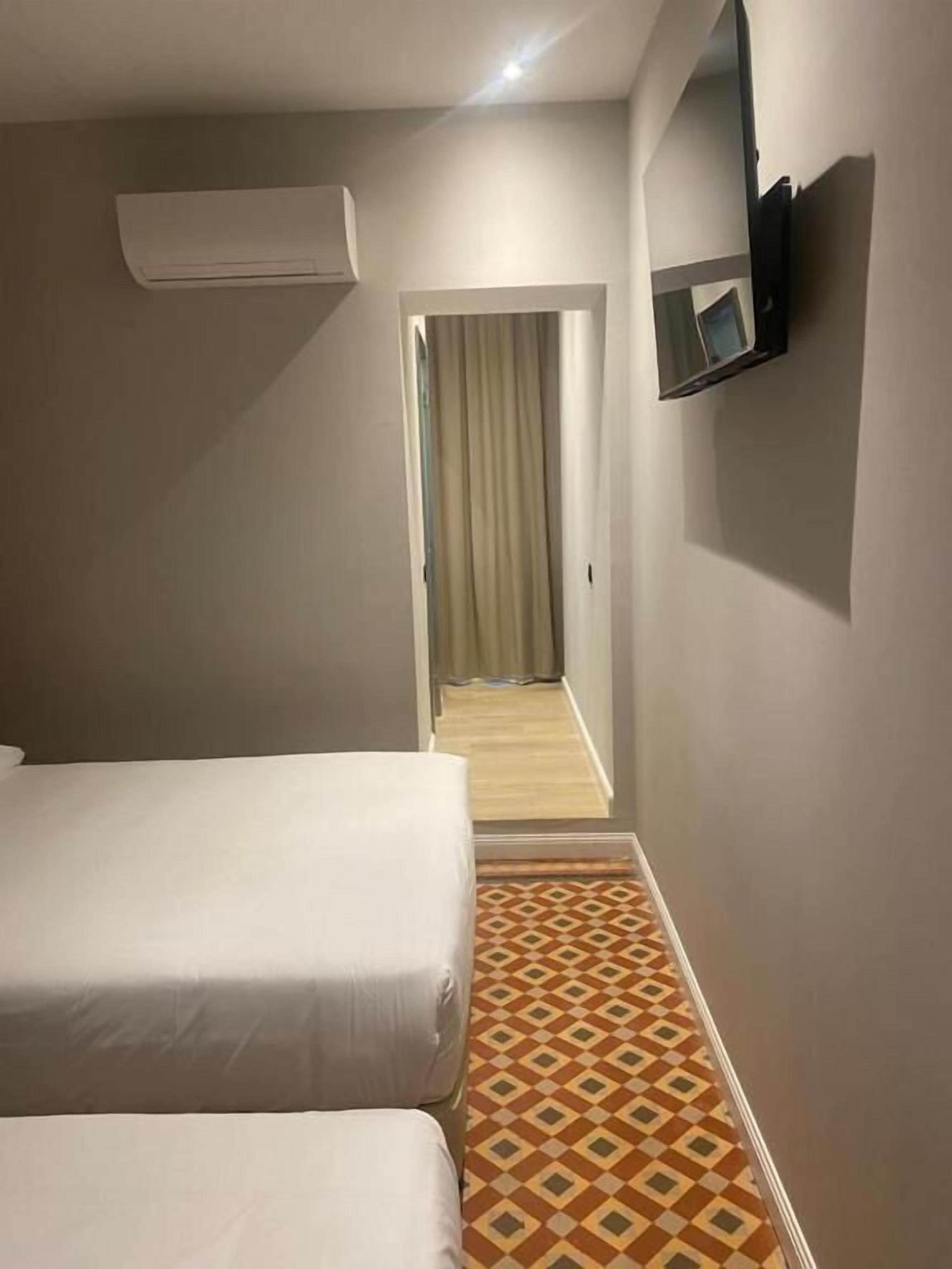 Une chambre d’hôtel avec deux lits, un téléviseur fixé au mur et un sol à motifs.