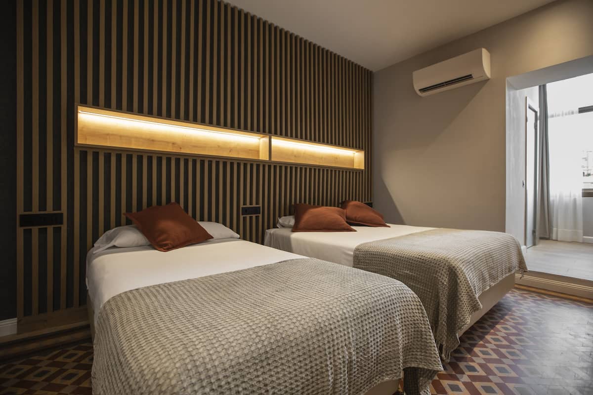Habitación de hotel con dos camas, un panel de pared de listones de madera, un equipo de aire acondicionado y un suelo estampado.