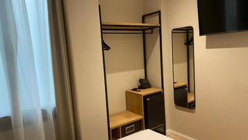 Una habitación de hotel con una cama, un escritorio con teléfono, un armario pequeño, un espejo y un televisor montado en la pared.