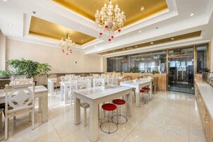 Un comedor amplio con varias mesas y sillas, un candelabro y una cocina moderna al fondo.