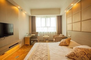 Ein Hotelzimmer mit Bett, Fernseher, Schreibtisch mit Stuhl, einem kleinen Tisch und einem Fenster mit Vorhängen.