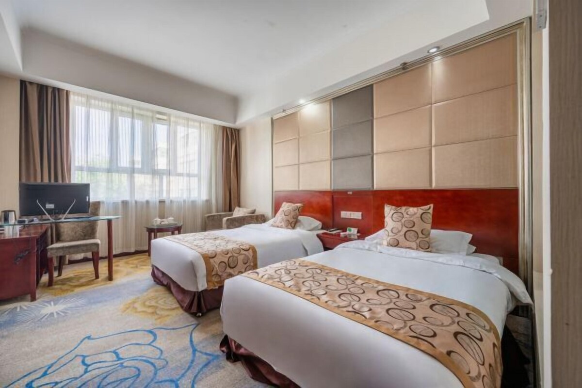 Een hotelkamer met twee bedden, een bureau met een televisie en een groot raam met gordijnen.
