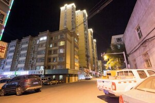 Vista nocturna de una calle con edificios, coches estacionados y un letrero muy iluminado.