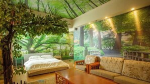 Quarto com cama, mesa de centro de madeira, sofá e um mural com uma paisagem de floresta.