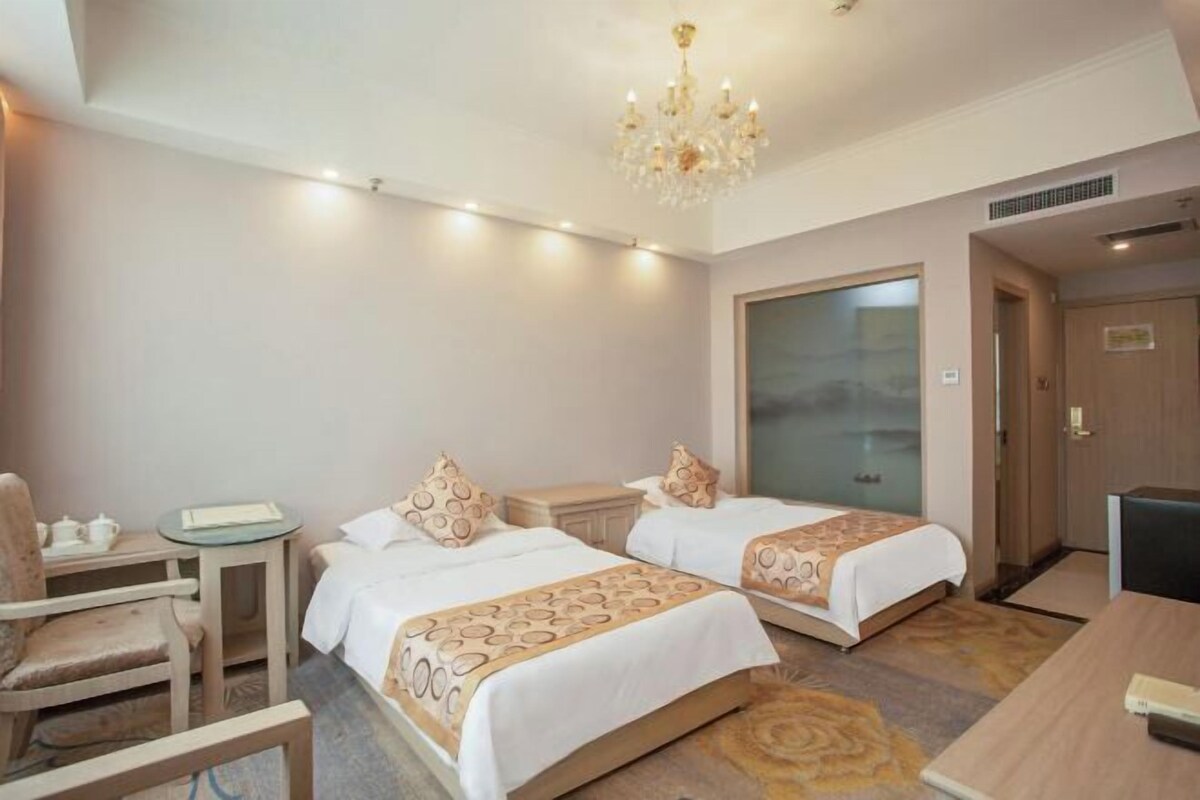 Een hotelkamer met twee bedden, een bureau, een stoel en een kroonluchter.