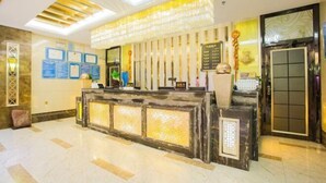 Uma área de recepção de hotel com piso de mármore, balcão de recepção com design em mosaico, certificados emoldurados na parede e um painel decorativo.