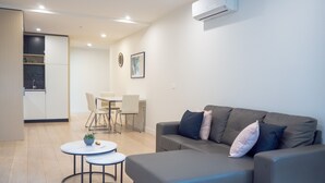 A modern living room with a grey sofa, two round tables, and a dining area with a white table and chairs. - Classy & Spacious 2 Bedroom, 2 Bathroom (En Suite) (Elsternwick)