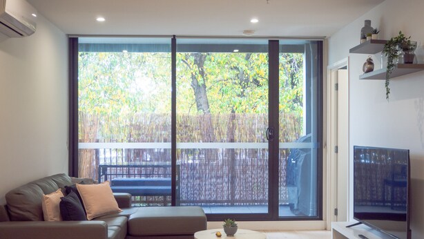 A modern living room with a sofa, a small round table, and a TV on a stand. - Classy & Spacious 2 Bedroom, 2 Bathroom (En Suite) (Elsternwick)