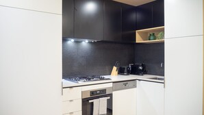 A modern kitchen with black and white cabinetry, a black tiled backsplash, a stove, a microwave, and a dishwasher. - Classy & Spacious 2 Bedroom, 2 Bathroom (En Suite) (Elsternwick)