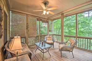 Relax in this serene space with a sofa, coffee table, and two wicker chairs on the wooden deck, surrounded by lush greenery.