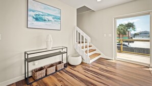 Ein modernes Interieur mit Holzboden, einer weißen Treppe, einem Konsolentisch mit Körben und einem großen Gemälde einer Welle.