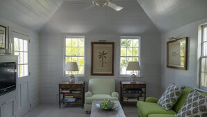 A room with a green sofa, a wooden coffee table with decorative items, a striped armchair, and a television on the left. - Charming Cottage in Harbour Island, minutes walk to Pink Sands beach (Dunmore Town)